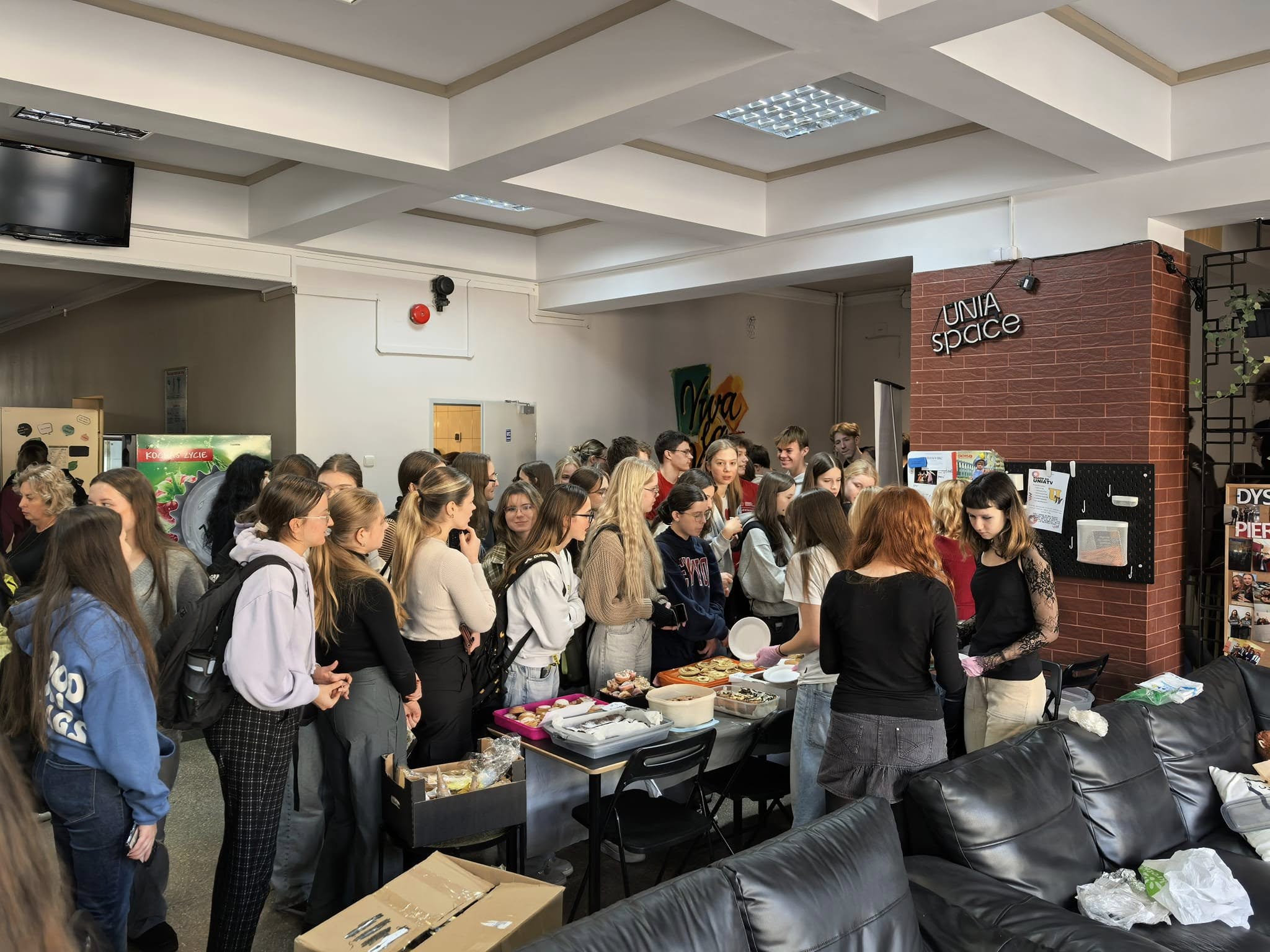 duża grupa młodzieży gromadzi się wokół stołu z przedmiotami na sprzedaż