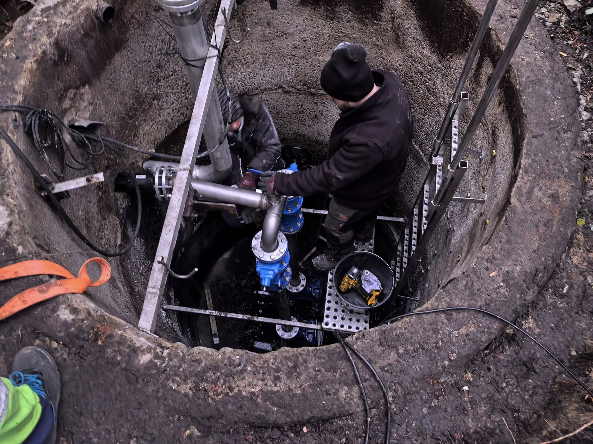 2 osoby znajdują się wewnątrz betonowej studni, w której znajdują się urządzenia przepompowni