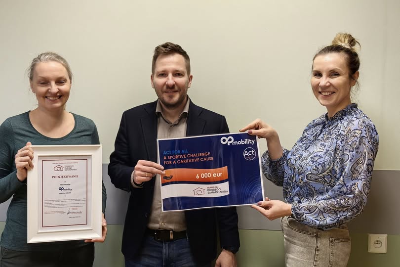 Dwie przedstawicielki firmy Plastic Omnium oraz przedstawiciel Hospicjum stoją na tle ściany trzymając w dłoniach dyplomy z podziękowaniami