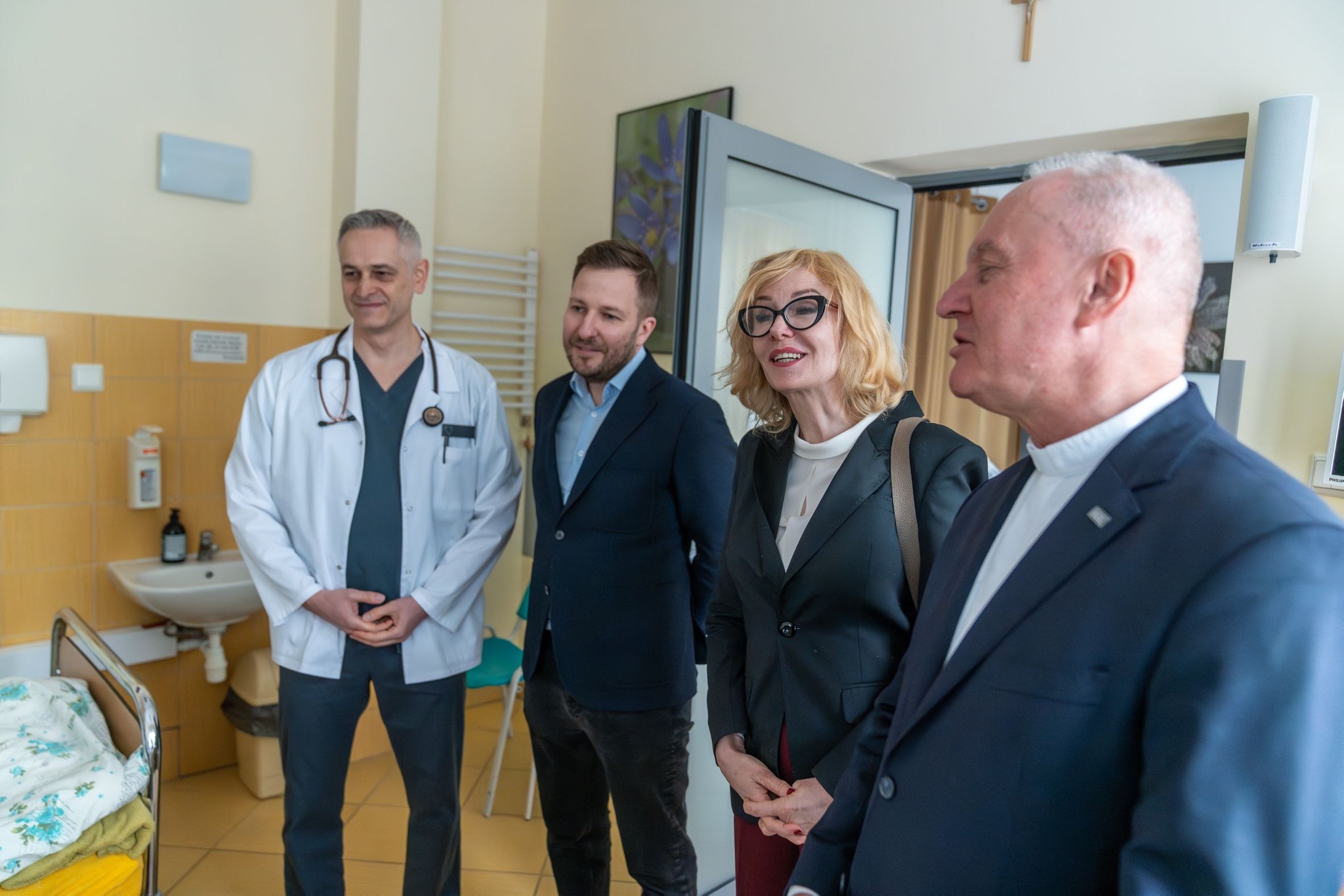 Trzej mężczyźni i kobieta stoją w pokoju chorych w Hospicjum